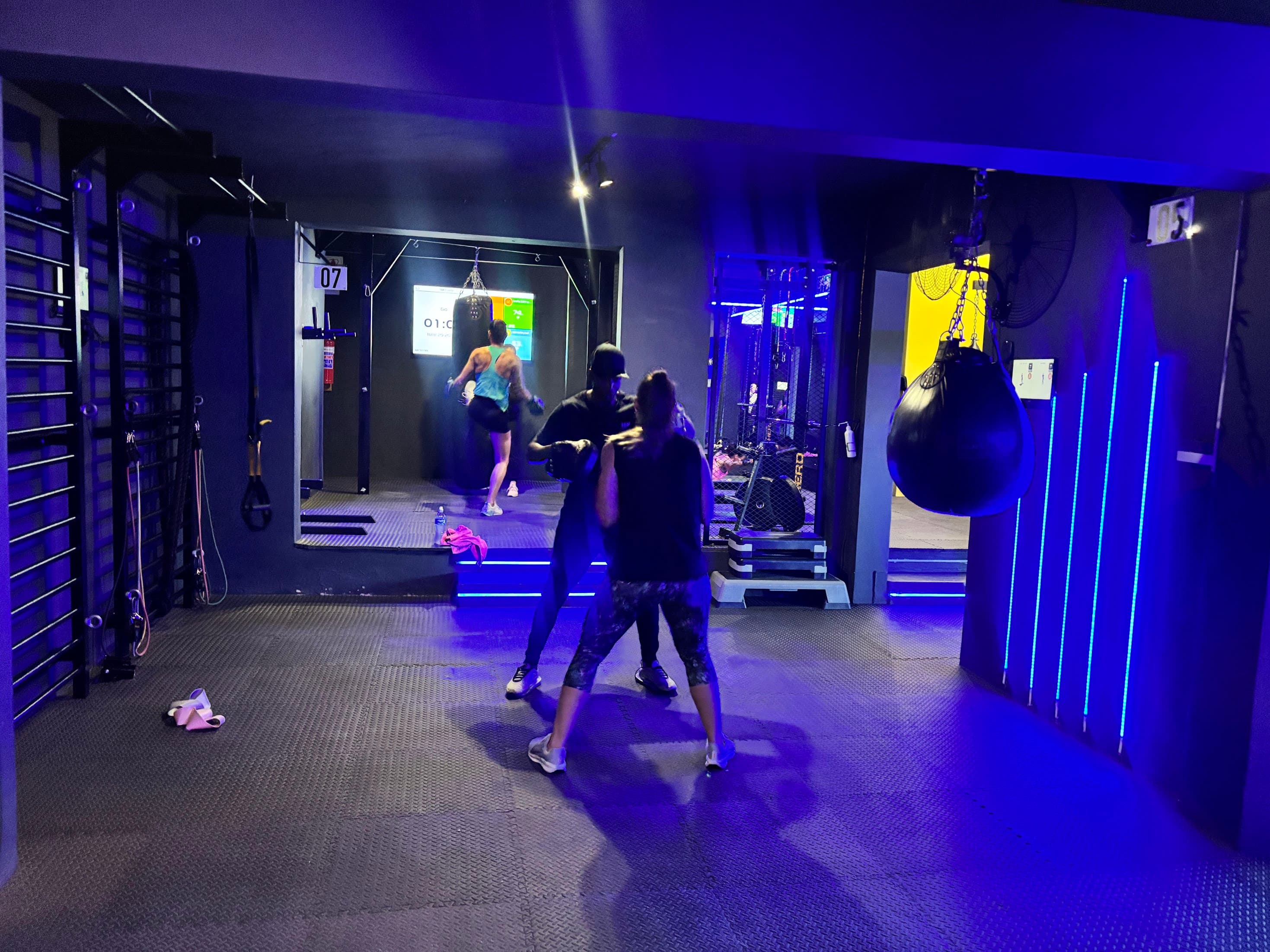 Coach holding pads for a member in the blue-lit station corridor during a TENROUNDS class