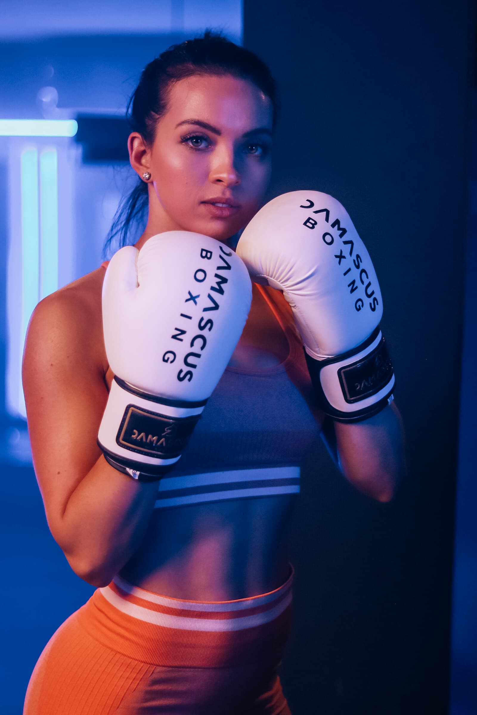 Female member holding a boxing guard stance with white gloves under blue gym lighting